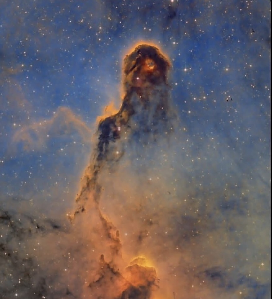 A tall column of dust and gas in a nebula, lit from within, against a field of stars.